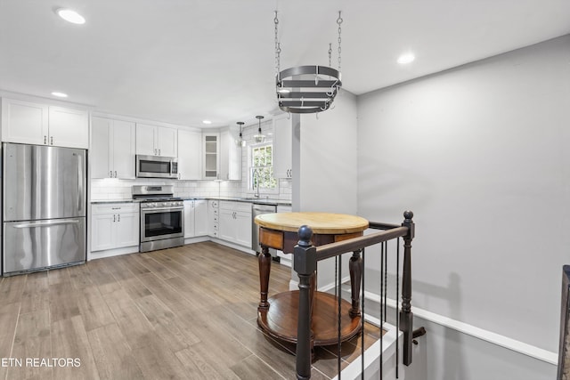 kitchen with white cabinetry, backsplash, pendant lighting, stainless steel appliances, and light wood-type flooring