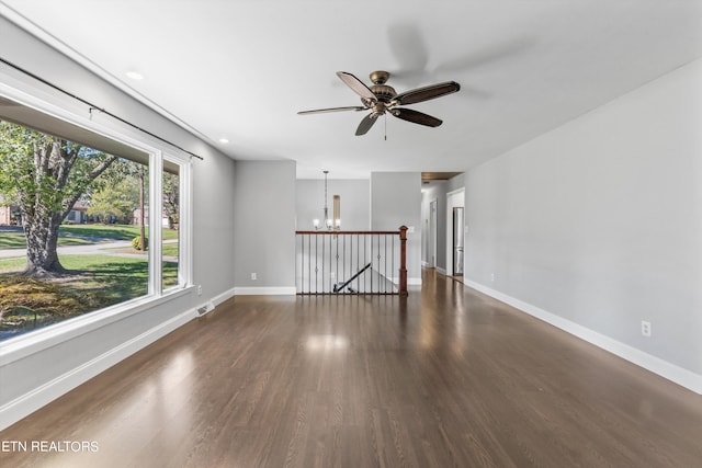 spare room featuring ceiling fan with notable chandelier and dark wood-type flooring