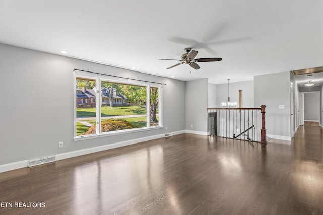 empty room with ceiling fan with notable chandelier and dark wood-type flooring