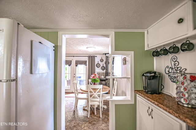 kitchen featuring white refrigerator, dark stone counters, crown molding, and white cabinetry