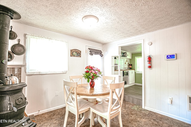 dining area featuring a textured ceiling, wood walls, and a wood stove