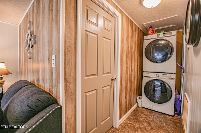 washroom with a textured ceiling, wooden walls, and stacked washer / drying machine