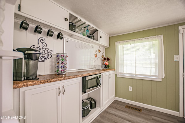 kitchen with white cabinets, wood-type flooring, stainless steel microwave, and a textured ceiling