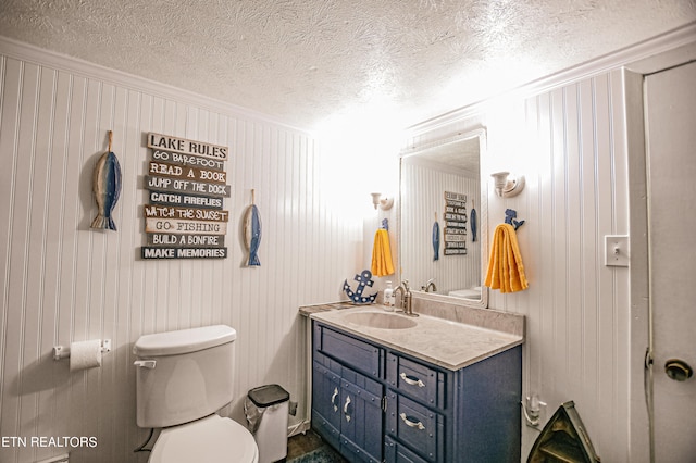 bathroom with vanity, a textured ceiling, wooden walls, crown molding, and toilet