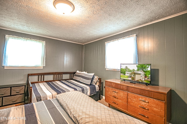 bedroom with a textured ceiling, wooden walls, crown molding, and multiple windows