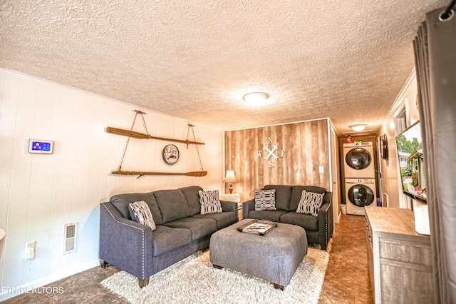 carpeted living room featuring a textured ceiling, wood walls, and stacked washing maching and dryer