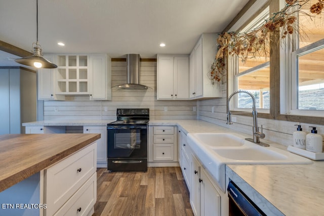 kitchen with hanging light fixtures, wall chimney range hood, white cabinets, and black range with electric cooktop