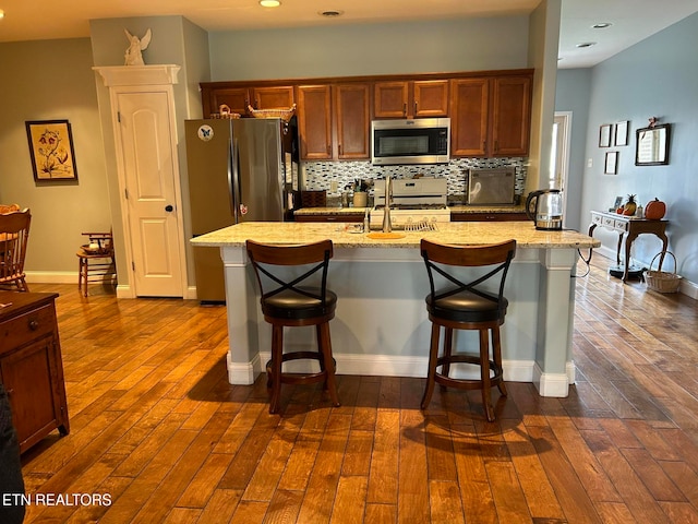 kitchen featuring an island with sink, dark hardwood / wood-style floors, a breakfast bar, sink, and appliances with stainless steel finishes