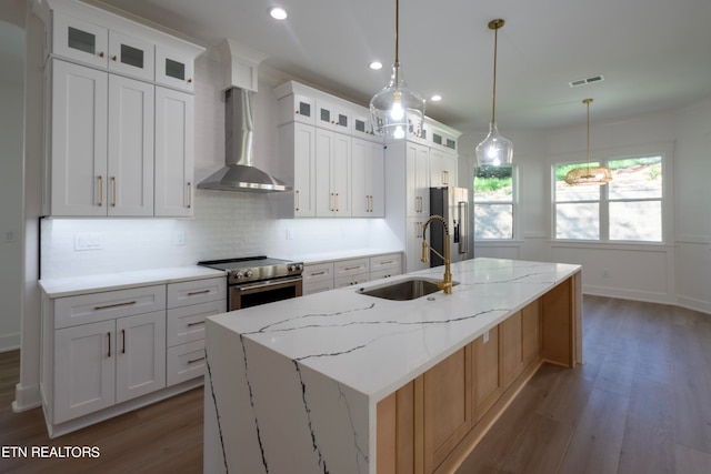 kitchen featuring visible vents, a center island with sink, a sink, appliances with stainless steel finishes, and wall chimney exhaust hood