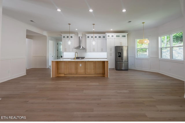 kitchen with stainless steel fridge with ice dispenser, a sink, light countertops, wall chimney exhaust hood, and light wood-type flooring