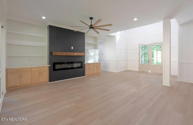 unfurnished living room with a ceiling fan, built in shelves, a fireplace, and light wood-style floors