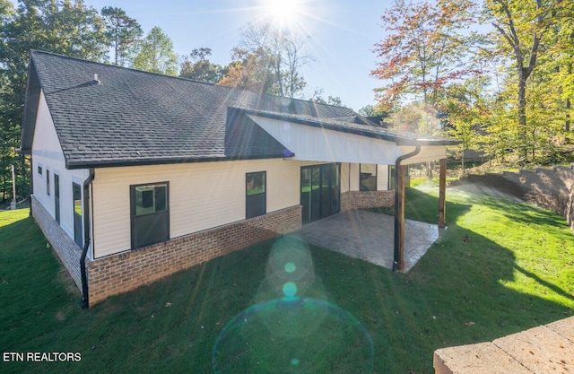 back of house featuring a lawn, a shingled roof, brick siding, a chimney, and a patio area