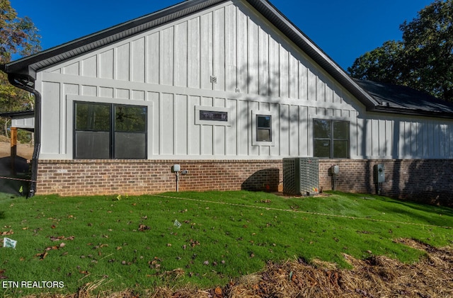 view of side of property with brick siding, board and batten siding, central AC, and a yard