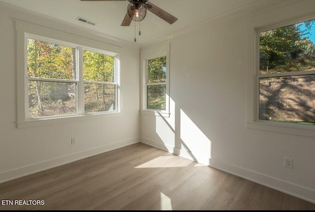 spare room featuring light wood finished floors, visible vents, a ceiling fan, and baseboards