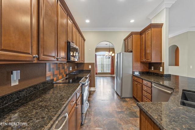 kitchen featuring an inviting chandelier, backsplash, appliances with stainless steel finishes, ornamental molding, and dark stone countertops