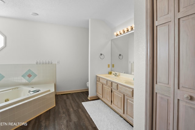 bathroom featuring a relaxing tiled tub, vanity, a textured ceiling, hardwood / wood-style flooring, and toilet