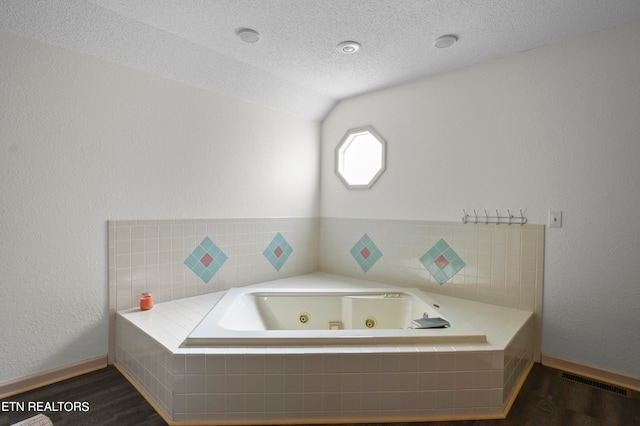 bathroom featuring vaulted ceiling, a relaxing tiled tub, hardwood / wood-style floors, and a textured ceiling