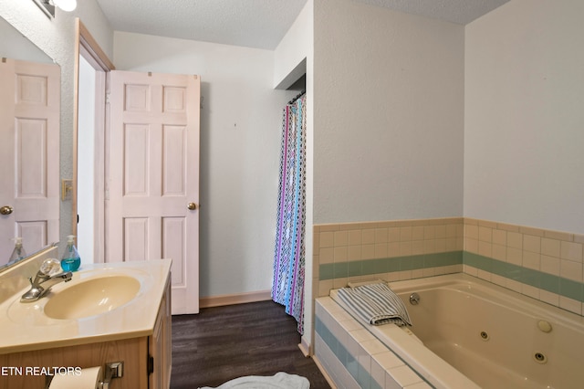 bathroom with a textured ceiling, tiled bath, hardwood / wood-style floors, and vanity