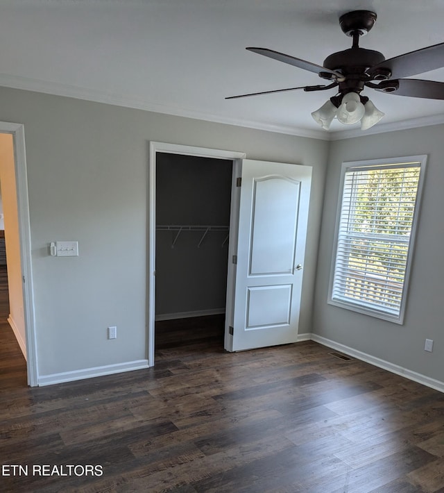 unfurnished bedroom featuring a closet, dark hardwood / wood-style floors, ornamental molding, a spacious closet, and ceiling fan