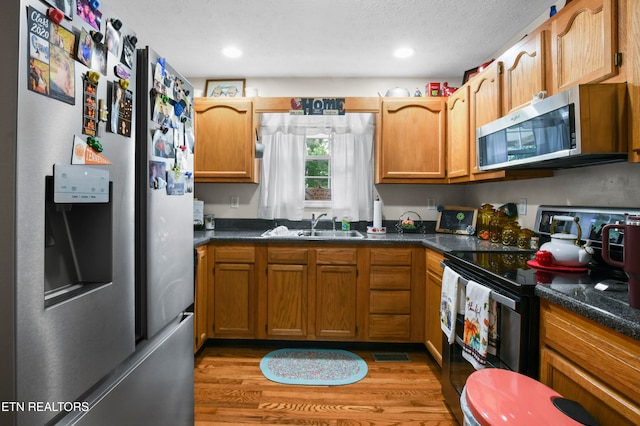 kitchen with sink, dark stone countertops, a textured ceiling, appliances with stainless steel finishes, and light wood-type flooring