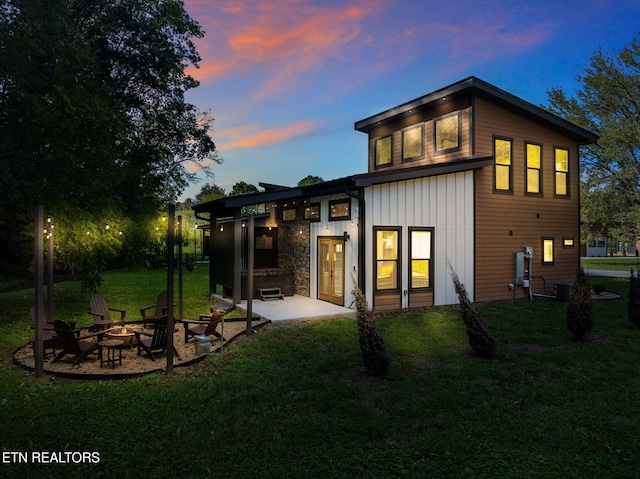 back of house at dusk featuring a fire pit, a yard, and a patio