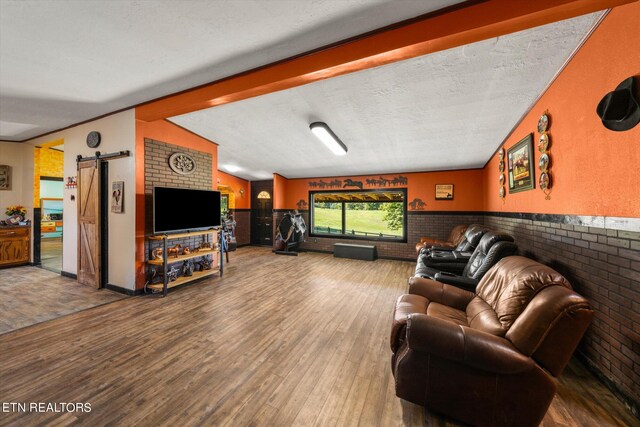 living room featuring lofted ceiling with beams, hardwood / wood-style floors, brick wall, a barn door, and a textured ceiling