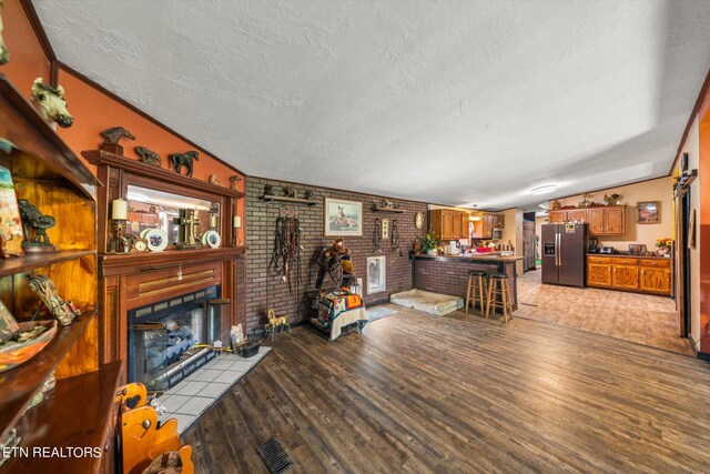 living room featuring lofted ceiling, brick wall, a textured ceiling, a fireplace, and light wood-type flooring