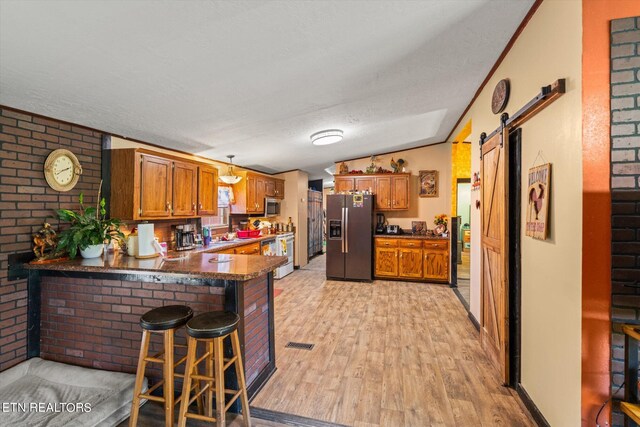 kitchen with a breakfast bar, light hardwood / wood-style floors, kitchen peninsula, vaulted ceiling, and appliances with stainless steel finishes