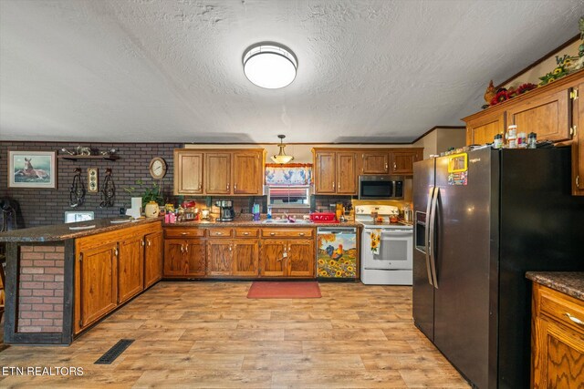 kitchen with kitchen peninsula, dark stone countertops, stainless steel appliances, and light hardwood / wood-style flooring