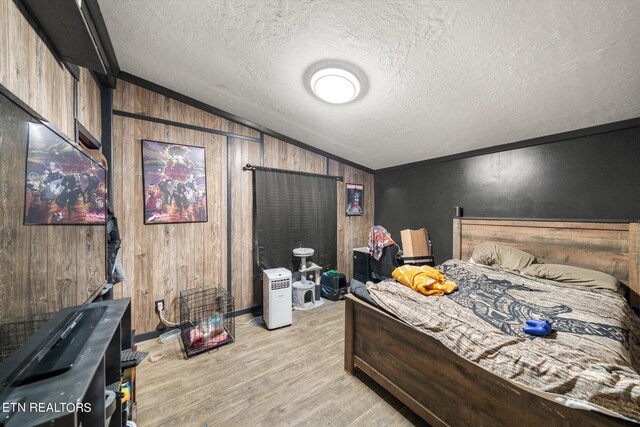 bedroom with light wood-type flooring, lofted ceiling, wood walls, and a textured ceiling