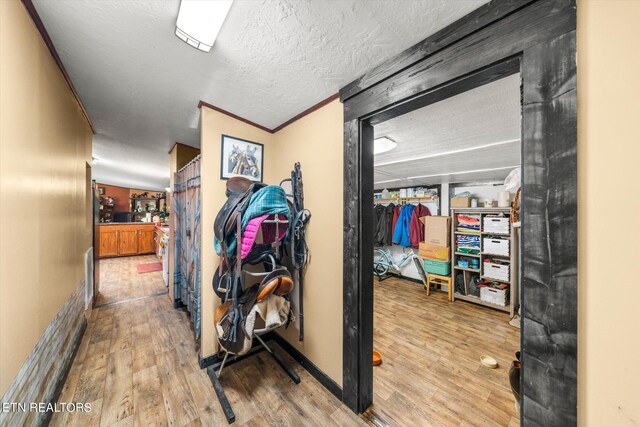 hallway featuring crown molding, light hardwood / wood-style floors, and a textured ceiling