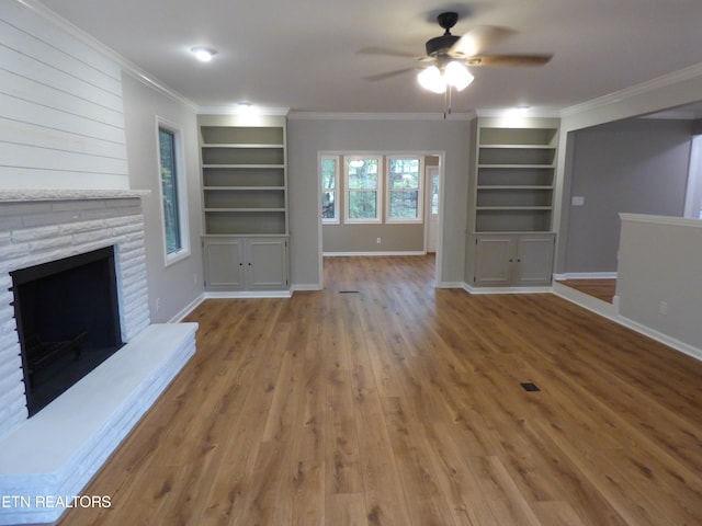 unfurnished living room with wood-type flooring, a stone fireplace, ornamental molding, and ceiling fan