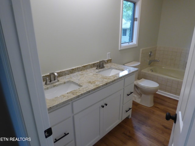 bathroom featuring tiled tub, vanity, hardwood / wood-style floors, and toilet