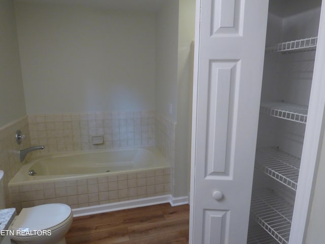 bathroom with hardwood / wood-style flooring, toilet, and a relaxing tiled tub