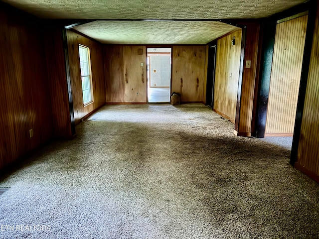 carpeted empty room with a textured ceiling and wood walls