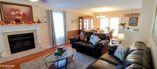 living room featuring an inviting chandelier, crown molding, a tiled fireplace, and hardwood / wood-style flooring