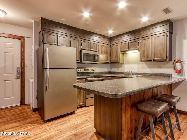 kitchen featuring a breakfast bar, stainless steel appliances, light hardwood / wood-style floors, and kitchen peninsula