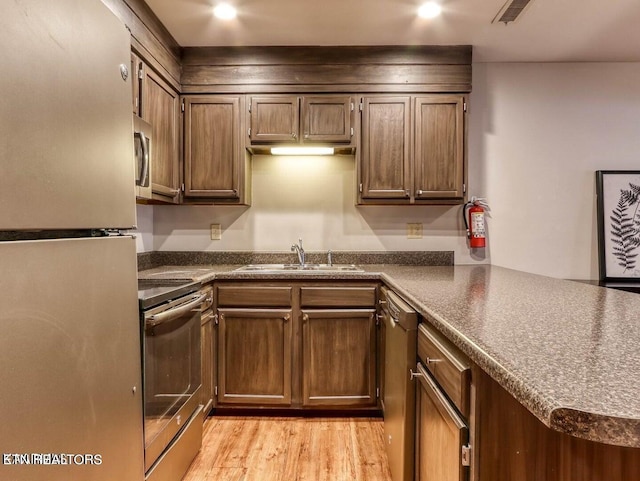 kitchen featuring sink, appliances with stainless steel finishes, light hardwood / wood-style floors, and kitchen peninsula