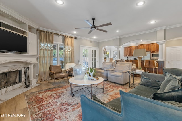 living room featuring light wood-type flooring, crown molding, a high end fireplace, and ornate columns