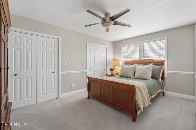 bedroom featuring ceiling fan, multiple closets, and light colored carpet