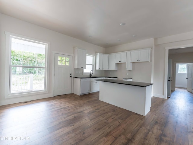 kitchen with white dishwasher, sink, a kitchen island, dark wood-type flooring, and white cabinetry