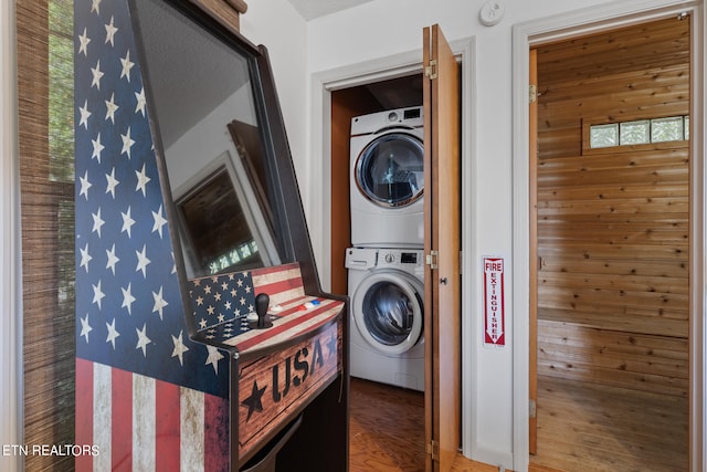 laundry area with wood walls, hardwood / wood-style flooring, and stacked washer / dryer