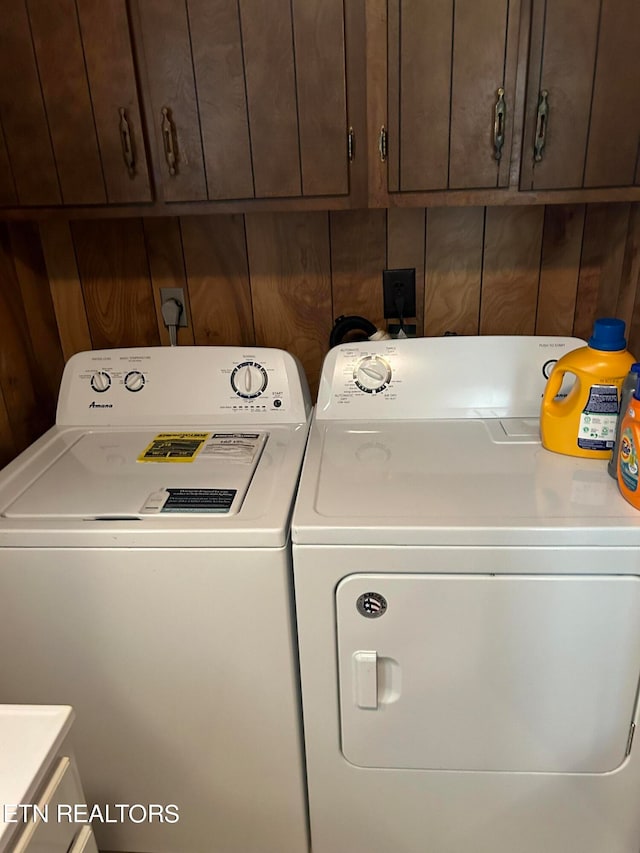 laundry area featuring washer and clothes dryer, cabinets, and wooden walls