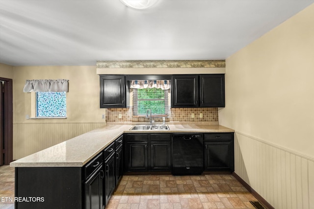 kitchen featuring black dishwasher, wood walls, plenty of natural light, and sink