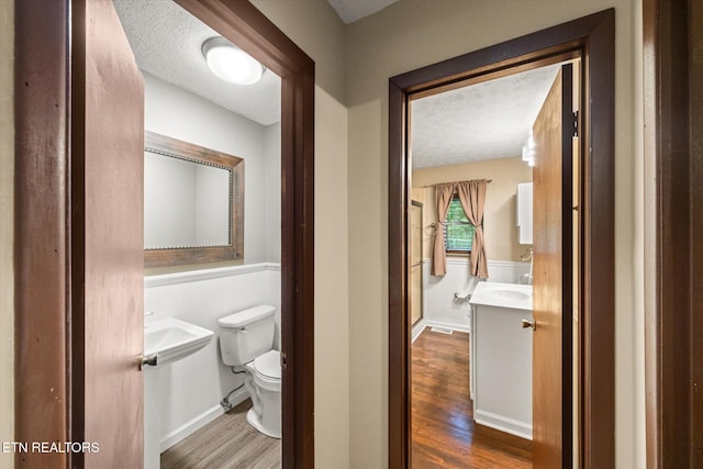 bathroom with a textured ceiling, vanity, toilet, and hardwood / wood-style flooring