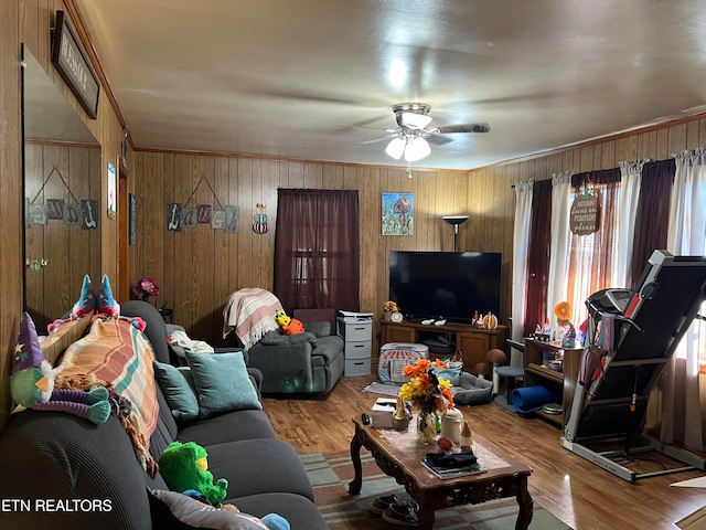 living room featuring ceiling fan, wood walls, ornamental molding, and light wood-type flooring