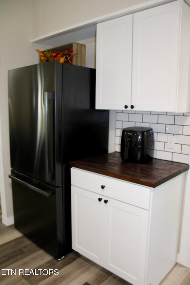 kitchen featuring wood-type flooring, butcher block countertops, stainless steel fridge, and white cabinetry