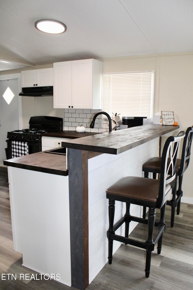 kitchen with white cabinets, kitchen peninsula, black range with gas cooktop, a kitchen breakfast bar, and light hardwood / wood-style floors