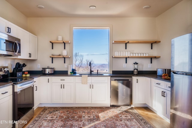 kitchen with stainless steel appliances, sink, light wood-type flooring, and white cabinetry