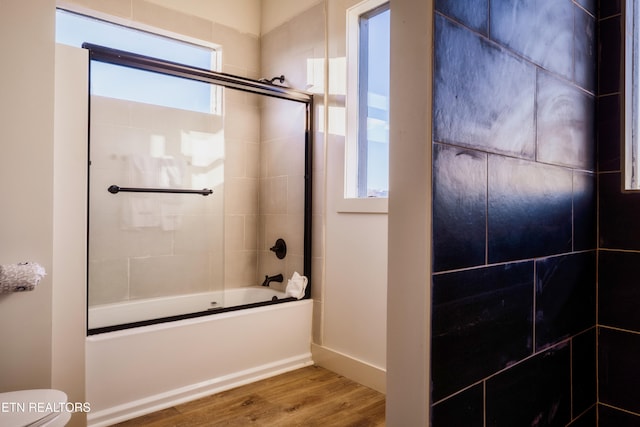 bathroom featuring hardwood / wood-style flooring, combined bath / shower with glass door, and toilet